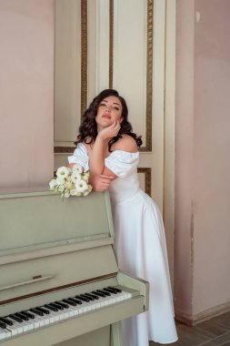 The bride leans on the piano and languidly looks into the lens