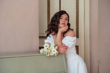 Portrait of young gorgeous bride with bouquet. Wedding day gatherings. The bride leans on the piano and languidly looks into the lens