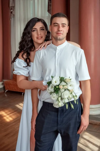 Happy new family. The bride gently snuggled up to the groom. Happy bride and groom. Portrait of a man and a woman in a white vintage dress in a classic interior on a wedding day.