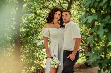 Couple in love summer forest against backdrop of dense greenery on Valentine's Day. View from bushes. Couple in love in white robes. Selective focus, blurred background, bokeh