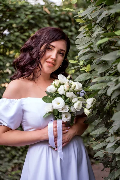 Portrait of happy bride with bouquet of white flowers and bare shoulders. Ukrainian black-haired newlywed. Selective focus