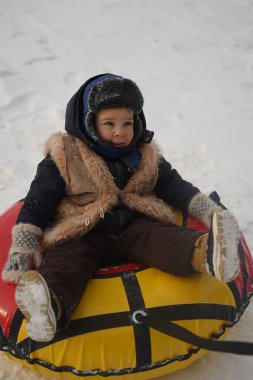 cute little boy in bright winter clothes sits on a tubing on a snow background, children's emotions, active winter family vacations with children.