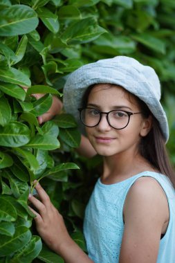 Portrait of a girl in a hat against the background of thick foliage.
