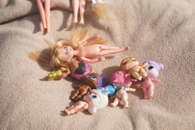 Lots of children's dolls on a beige bedspread, top view.