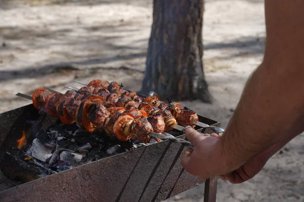 Backyard barbecue. Mans hands grilling kebab on metal skewer fresh meat.