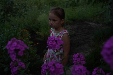 Cute girl child model in the garden between flowers at sunset. Selective focus.