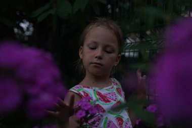 Cute girl child model in the garden between flowers at sunset. Selective focus.