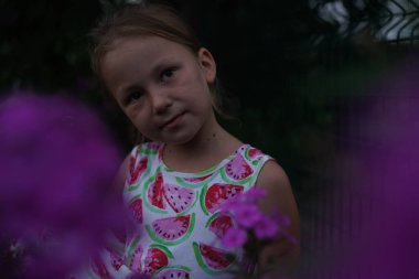 Cute girl child model in the garden between flowers at sunset. Selective focus.