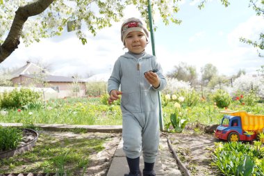 A cheerful baby in the village against the background of a vegetable garden and children's toys. Spring children's games.