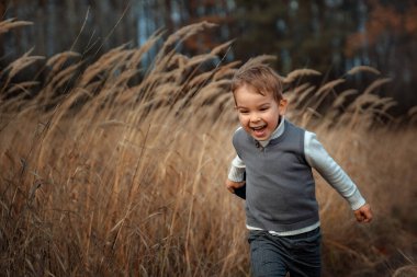 A little boy in fashionable retro clothes runs across the field with a cheerful scream and happiness on his face. Portrait of happiness with copy space
