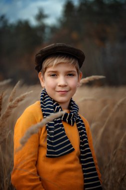A smiling little boy in a retro style cap stands and smiles. Children's fashion, retro style.