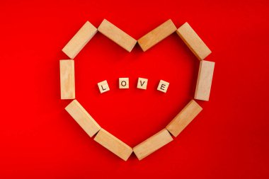 The word LOVE made of wooden letters of the alphabet on a red background, framed by a frame in the shape of a heart made of wooden bricks. The concept of love and valentine's day, happy family, wedding, fidelity