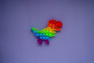 Pop It Dinosaur , a toy for children to train their concentration and relieve stress. Very Peri background. Top view, copy space.