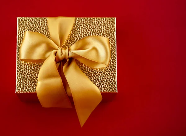 Golden gift box with a large golden bow on a red background top view
