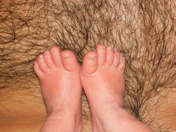 Newborn baby\'s feet on a hairy male chest close-up. Baby\'s legs on the father\'s breast. Soft focus.