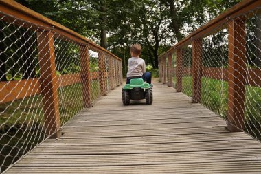 Oyuncak bir arabayla tahta bir köprüden geçen bir çocuk. Dikiz manzarası. Bağımsız bir çocuk dünyayı keşfeder..