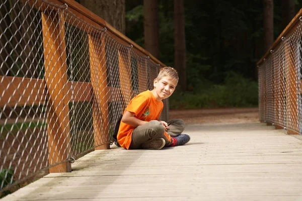 Ένας Χαρούμενος Έφηβος Κάθεται Μια Ξύλινη Γέφυρα Στο Δάσος Στη — Φωτογραφία Αρχείου