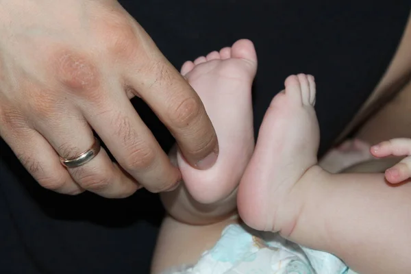 Children\'s feet in hands of father. Dad tickles feet of kid. Baby counts toes. Happy father.