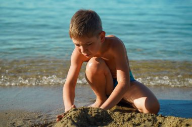 Bir çocuk deniz kıyısında bir kumdan kale inşa ediyor, yakın plan bir portre.