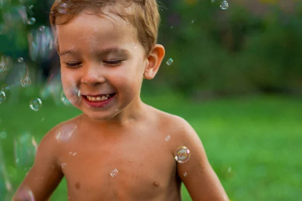 stock image A little boy without clothes happily stands in a stream of flying soap bubbles.