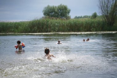Küçük bir çocuk suda oynar ve su sıçratır. Bir çocuk gölde ya da nehirde yüzer ve damlalarla eğlenir. Seçici odak.
