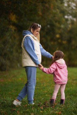 Genç anne küçük kızıyla yeşil alanda yürüyor. Bahçede aile tatili. Doğada çocuklu anne portresi. Anne, küçük kızım dışarıda. Anneler Günün kutlu olsun. Kapat..