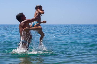 Baba, oğlunu denize fırlattı. - Ne? Babam denizde çocuklarla oynardı. Çocuk zıplıyor ve denizde uçuyor. Yumuşak odak.