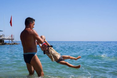 Baba, oğlunu denize fırlattı. - Ne? Babam denizde çocuklarla oynardı. Denizde uçan çocuk. Yumuşak odak.