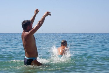 Baba, oğlunu denize fırlattı. - Ne? Babam denizde çocuklarla oynardı. Çocuk zıplıyor ve denizde uçuyor. Yumuşak odak.