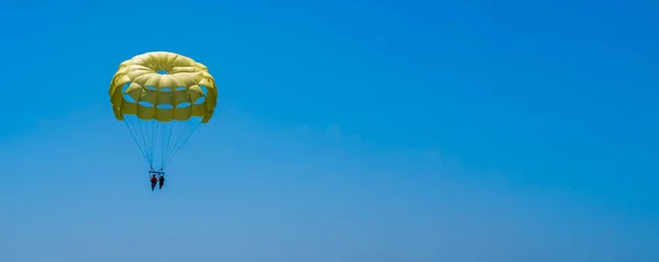 Parasailing on a yellow parachute against the blue sky. Beach extreme adventures. Background vacation, photo for postcards, tourist and travel guide. The concept of summer holidays, vacation, tourism.