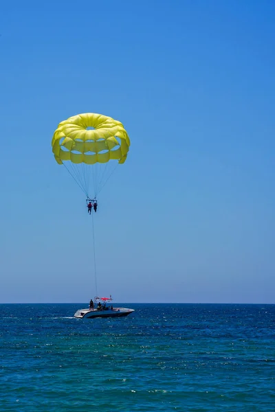Parasailing on a yellow parachute against the blue sky. Beach extreme adventures. Background vacation, photo for postcards, tourist and travel guide. The concept of summer holidays, vacation, tourism.