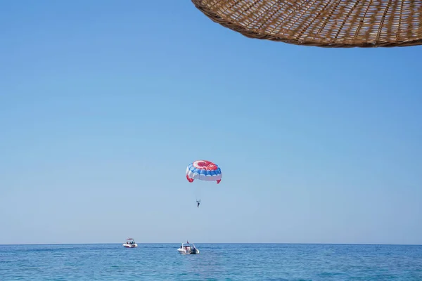 Parasailing on a parachute against blue sky. Background vacation, photo for postcards, tourist and travel guide. Concept of summer holidays, vacation, tourism. View from under umbrella. Soft focus.