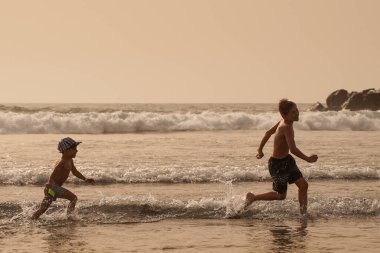 Çocuklar sahilde deniz kenarında koşarken eğleniyor. Kardeşler birbirini kovalıyor..