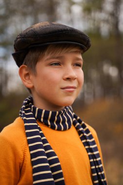 Retro şapkalı şirin bir gencin portresi ve sonbahar ormanının arka planında çizgili bir eşarp.