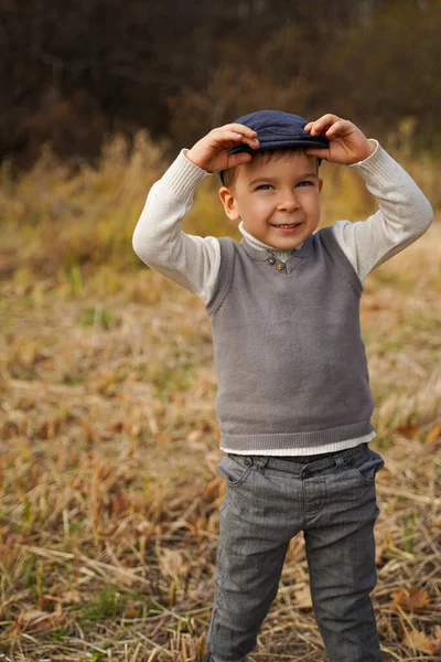 戴着帽子的可爱男孩站在田里笑着 一个穿着旧衣服的男孩 — 图库照片