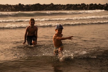 Çocuklar sahilde eğleniyor, her yöne sıçrıyor. İyi tatiller. Eğlenceli bir tatil. Aile Deniz Tatili