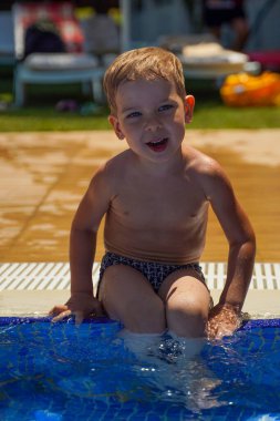 Havuzun kenarında oturan neşeli bir çocuk. Eğlenceli bir yaz tatili. Aile Tatili