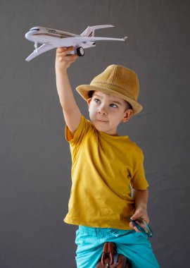 Yazlık şapkalı bir çocuk bir bavula oturur ve yükseltilmiş elinde bir uçak tutar. Yaz tatili kavramı