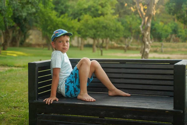 Ένα Αγόρι Κάθεται Ένα Παγκάκι Ένα Καλοκαιρινό Πάρκο Σορτς Και — Φωτογραφία Αρχείου