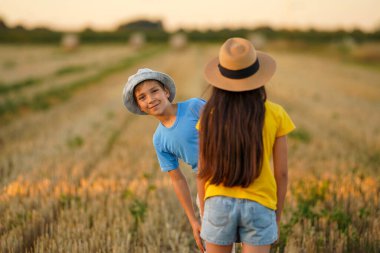 Uzun saçlı bir kız arkasında duruyor, bir adam arkasından bakıyor ve gülümsüyor. Birbirine aşık bir çift doğada eğleniyor.