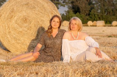 Anne ve kızı yazın tarlada oturuyor. Mutlu anne ve küçük kızı ayçiçeği tarlasında