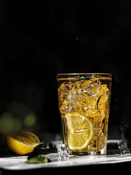 Siyah zemin üzerinde buz küpleri olan bir bardak limon suyu.