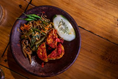 Geleneksel taş havan topu içinde acı biber soslu, hıyarlı ve sebzeli Tempeh Penyet tipik Endonezya yemeği.