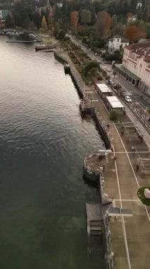 İtalya 'nın kuzeyindeki Stresa Lago Maggiore' a giden dikey İHA video uçuşu, geleneksel kırmızı çatı binalarıyla çevrili ana göl yolunda hareket eden araçlar.  