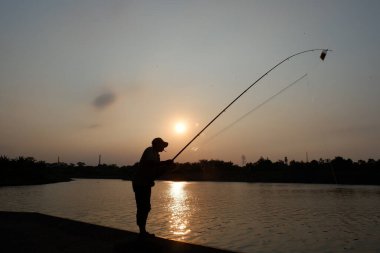 Citarum River, Karawang, August 2021 - A man is fishing in the afternoon with beautiful sunset in Citarum River, Karawang, Indonesia