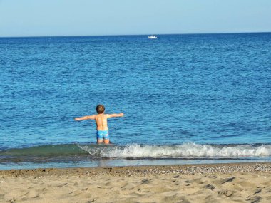 Çocuk plajda mavi mayosuyla oynuyor.