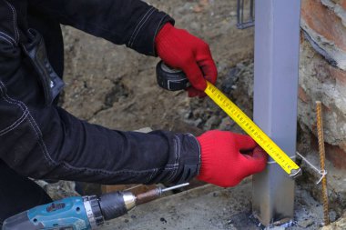 Metal yapıların kurulumuna başlamadan önce ölçüm yapan bir işçinin yakın çekimi. Yeni bir evin inşaatı.