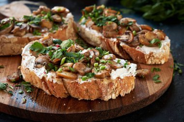 İştah açıcı bruschetta krem peyniri ve kızarmış şampiyon mantarı. Tahta kesme tahtasındaki taze otlarla süslenmiş..