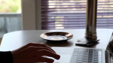 Bir adam dizüstü bilgisayarda çalışıyor ve sabah mutfağında sıcak kahve içiyor. Uzaktan çalışma ve serbest çalışma kavramı.