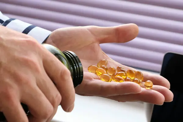 Close-up man pours medical pills, fatty acids, omega-3 vitamins into the palm of his hand. Medical capsules of yellow transparent color. Selective focus.